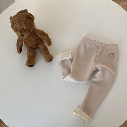 Fleece-lined girls leggings in beige color displayed with a plush teddy bear on a table.