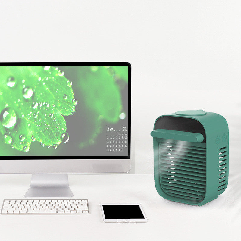 Desktop air conditioner fan with water spray beside a computer and tablet on a bright workspace.