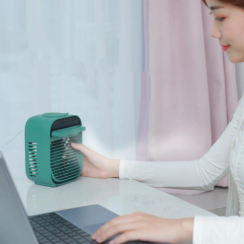 Woman using a desktop air conditioner fan with water spray at her workspace, promoting cool comfort.