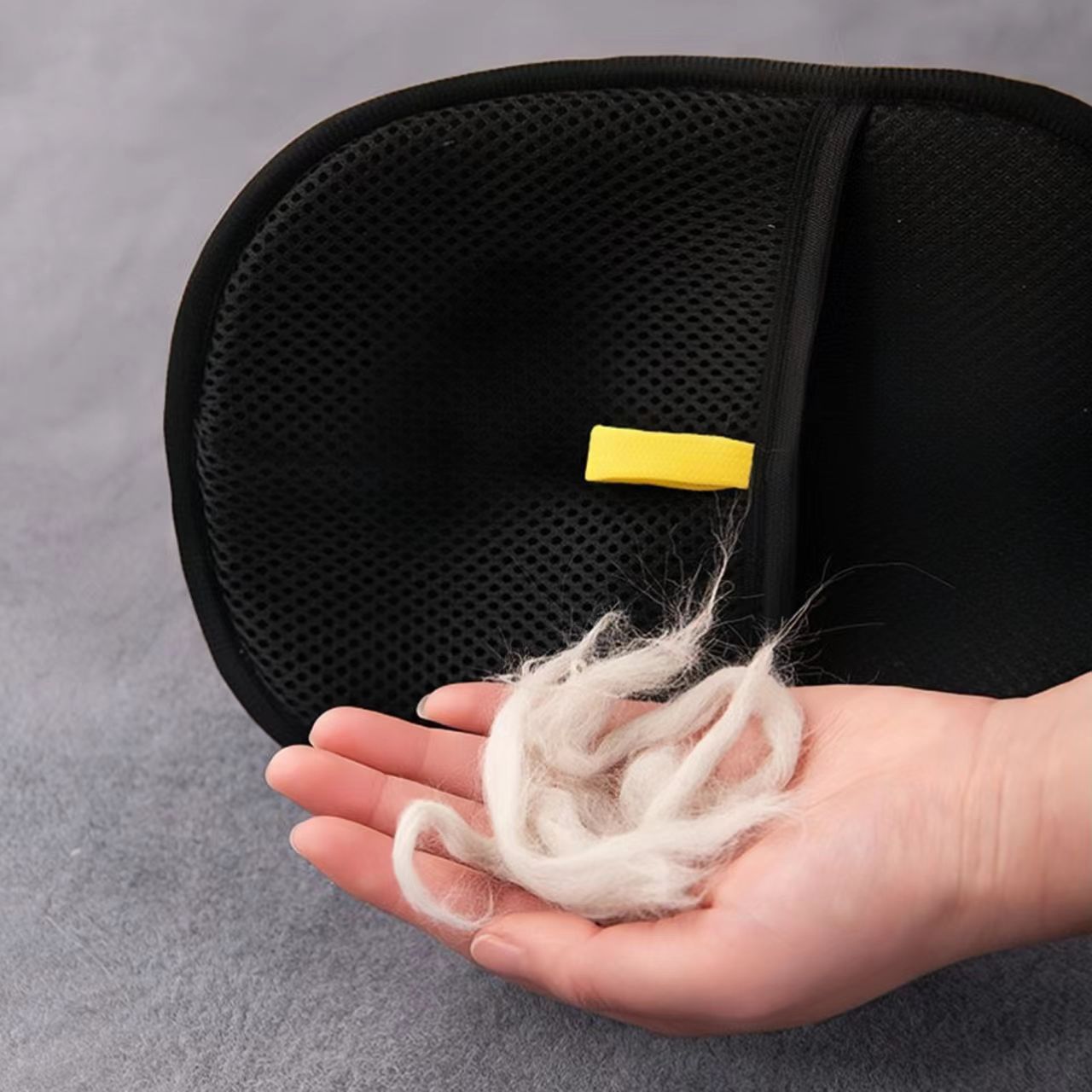 Hand holding pet hair near black electrostatic hair removal gloves for pets.