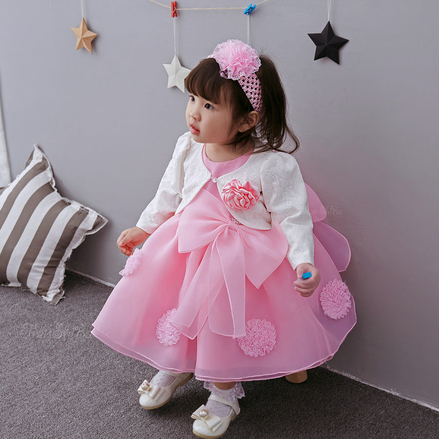 Girl wearing a pink princess dress for girls with flower details and a matching headband, sitting near decorative stars.