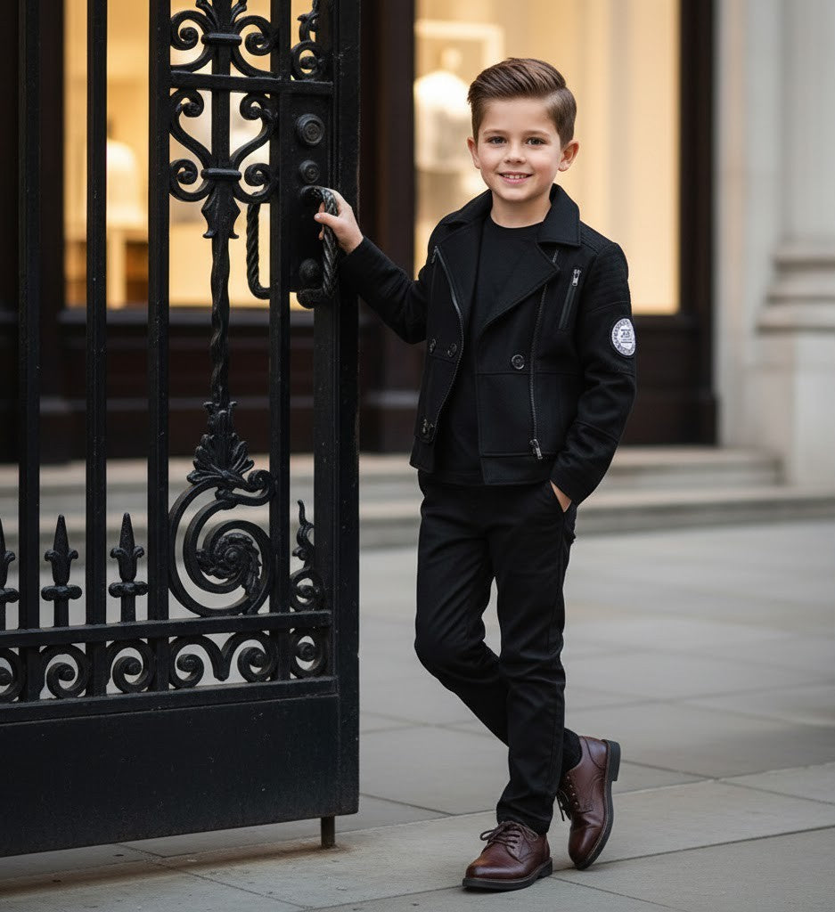 Boys military style jacket worn by a stylish young boy, posing confidently by an ornate gate.