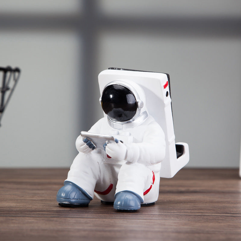 Cute astronaut phone stand designed as a spaceman holding a mobile device, perfect for desk decoration.