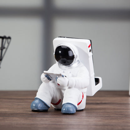Cute astronaut phone stand designed as a spaceman holding a mobile device, perfect for desk decoration.