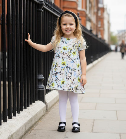 Toddler girls floral smock dress with puff sleeves worn by a happy girl outside on a city street.