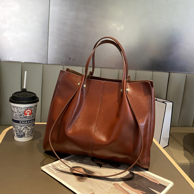 High-end leather tote bag in dark brown color placed on a table next to a coffee cup and magazines.