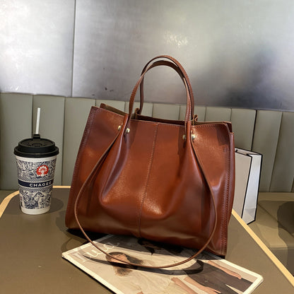 High-end leather tote bag in dark brown color placed on a table next to a coffee cup and magazines.