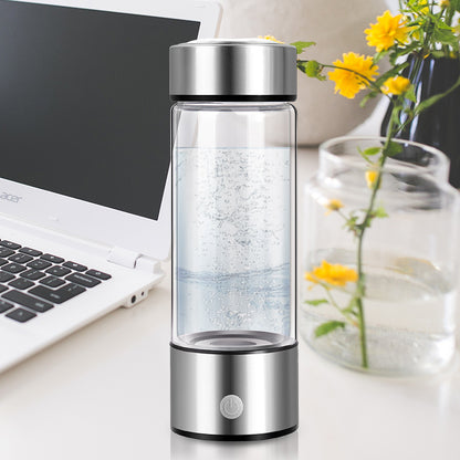 Hydrogen water generator bottle next to a laptop and flowers, showcasing its sleek design and functionality.