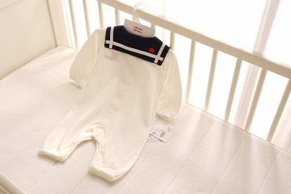 Navy style baby onesies in white with a navy collar on a crib mattress, perfect for newborn comfort.