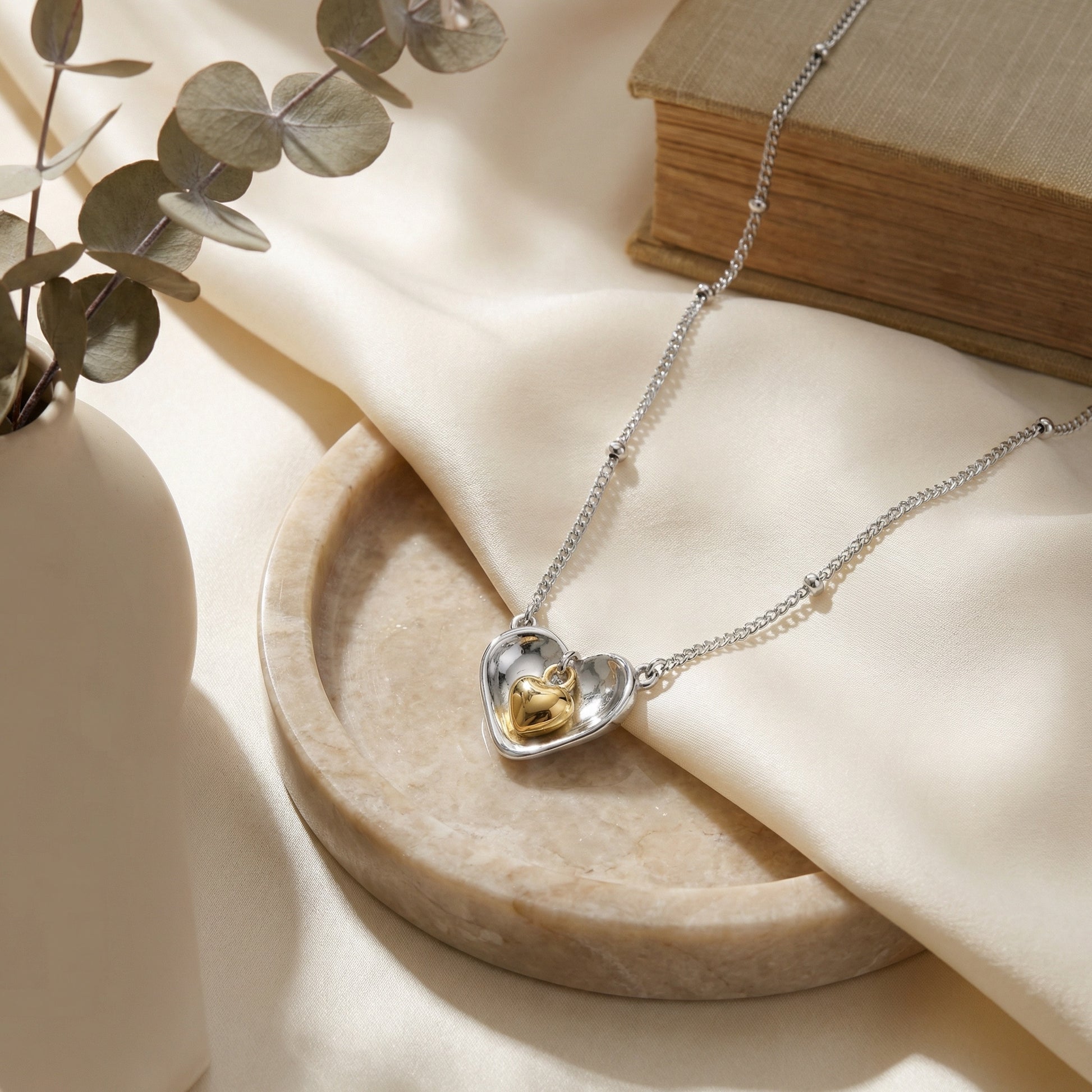 925 Sterling Silver nested heart pendant necklace on a marble dish with a book and eucalyptus.