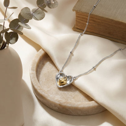 925 Sterling Silver nested heart pendant necklace on a marble dish with a book and eucalyptus.