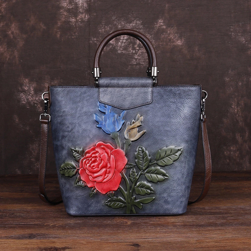 Vintage leather tote bag with floral design, featuring red rose and blue flower on a textured gray background.