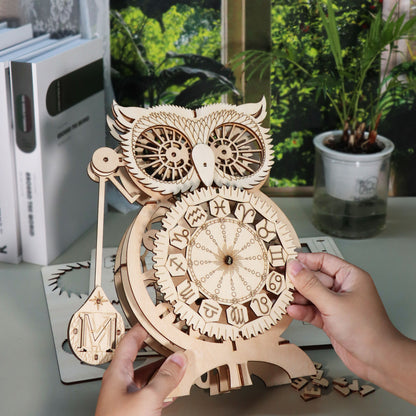Hands assembling the wooden owl clock puzzle kit by MUSIC PARK, showcasing intricate designs and craftsmanship.
