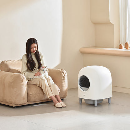 woman sitting on sofa with cat beside a fully automatic smart cat litter box in modern interior decor