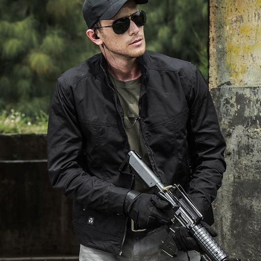 A man in black windproof military style jacket wearing sunglasses and holding a rifle outdoors.